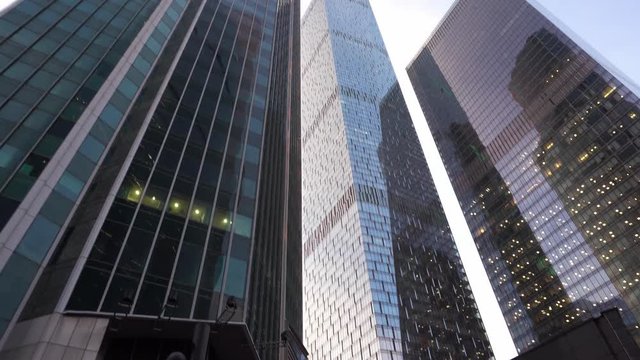 Modern, skyscrapers made of glass. View from below with rotation. In the background, a beautiful blue sky with white clouds and a plane flying in the distance. Daytime, close-up, no people