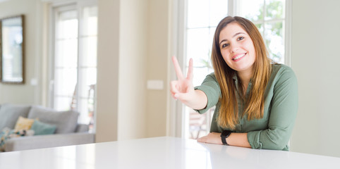 Beautiful young woman at home smiling looking to the camera showing fingers doing victory sign. Number two.