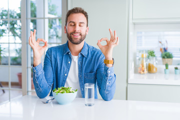 Handsome man eating fresh healthy salad relax and smiling with eyes closed doing meditation gesture with fingers. Yoga concept.