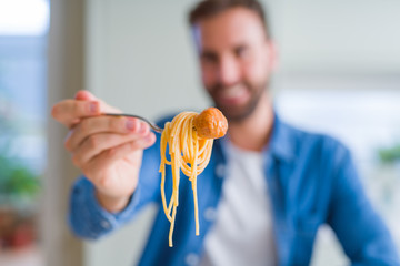 Handsome man eating pasta with meatballs and tomato sauce at home while smiling at the camera