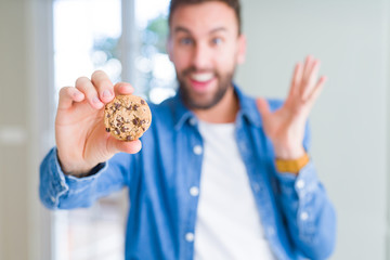 Handsome man eating chocolate chips cookies very happy and excited, winner expression celebrating victory screaming with big smile and raised hands