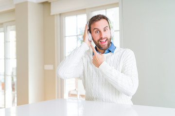 Handsome man wearing headphones and listening to music very happy pointing with hand and finger