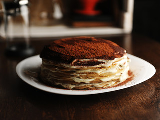 Crepe cake with tiramisu filling dusted with powdery cocoa. White plate, background of coffee house. Side view