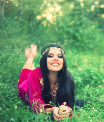 happy attractive cheerful woman with long black hair lying on the early grass, bright sunshine and glare, with wide smile resting in meadow, wise healer collects medicinal herbs