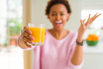 Young african american woman driking orange juice at home very happy and excited, winner expression celebrating victory screaming with big smile and raised hands