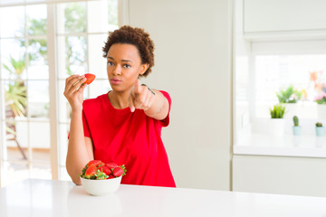 Young african american woman eating fresh strawberries for breakfast pointing with finger to the camera and to you, hand sign, positive and confident gesture from the front