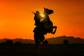 Fototapeta na wymiar Silhouette Cowboy holding short gun and riding a horse