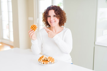 Senior woman eating sweet belgian waffle very happy pointing with hand and finger