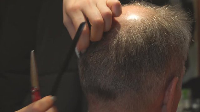 Woman hairdresser cuts a man with a receding hairline with scissors. Selective focus