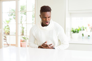 Handsome african american man on white table with hand on stomach because indigestion, painful illness feeling unwell. Ache concept.