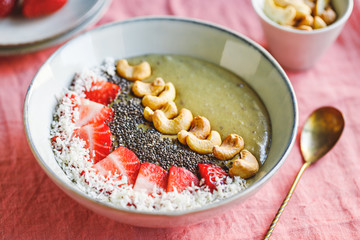 Green smoothie bowl with coconut cream, banana, strawberry, cashew and chia seeds. Healthy vegan eating.