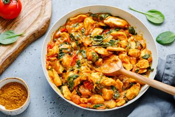 Bombay chicken curry with spinach, tomato and onion in a white frying pan on a kitchen table. Indian traditional cuisine.