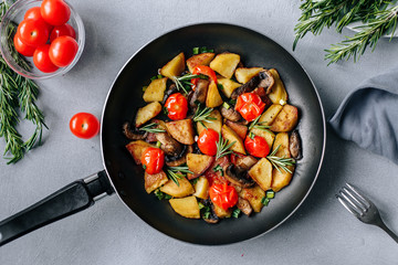 Fried potatoes in a pan with tomatoes, mushrooms,greens decorated with sprigs rosemary on a  table...