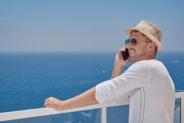 European man in a sunhat and sunglasses is talking on mobile phone, while having a rest at the beautiful resort. He is sharing his emotions.