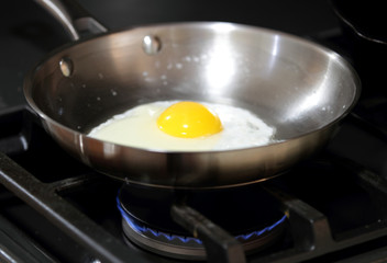 Egg sunny side up frying in a pan.