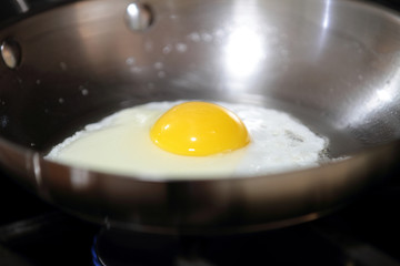 Egg sunny side up frying in a pan.