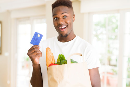 African american man holding paper bag full of groceries and holding credit card as payment