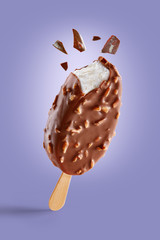 Chocolate covered ice cream with nuts on a purple background  bitten on top with chocolate bits. Taste explosion