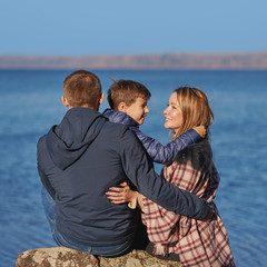 Young beautiful woman and her family are sitting near the picturesque lake. They are enjoying their trip and the atmosphere around.