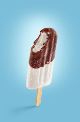 Brown and white ice cream on a stick isolated on a blue background. Chocolate popsicle bitten on top