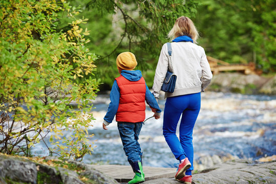 Mom and son are strolling along the picturesque path in the fir forest. They are enjoying wonderful view and fresh air.