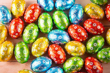 Many small dessert eggs in colored foil laying on table