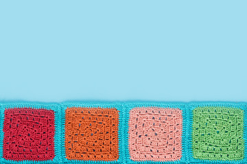  crocheted  lace tablecloth of multicolored squares ornament on a blu background, top view, place for text, natural wool