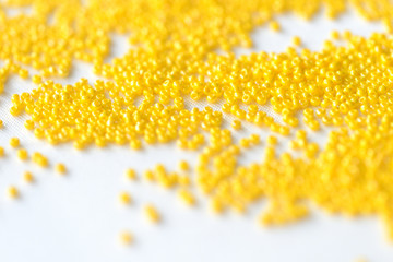 Seed beads yellow color scattered on a textile background close up