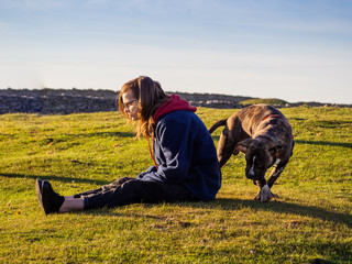 An teenager woman playing with a young dog of the American staffordshire breed in countryside in...