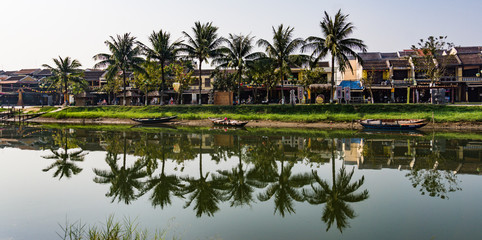 Fototapeta na wymiar Palm trees along river in old Hoi An reflected in water 