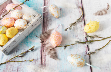Easter eggs in a wooden box with willow and feathers, view from the top