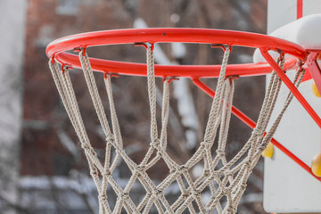 A beautiful red basketball hoop with white rope net and white snow on the children's playground in...