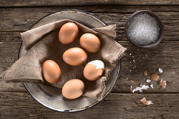 Cooked brown eggs on plate with coarse salt on the side, photographed overhead on wood (Selective...