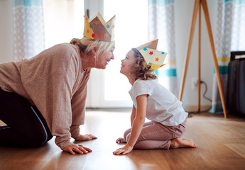 A portrait of small girl with grandmother having fun at home. - obrazy, fototapety, plakaty
