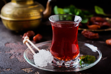 Turkish tea in traditional glass cup with caramelized sugar and mint on dark background. Selective focus.