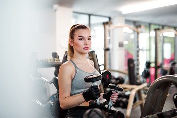 Fototapeta premium Young girl or woman with dumbbells, doing workout in a gym.