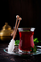 Turkish tea in traditional glass cup with caramelized sugar and mint on dark background. Selective focus.