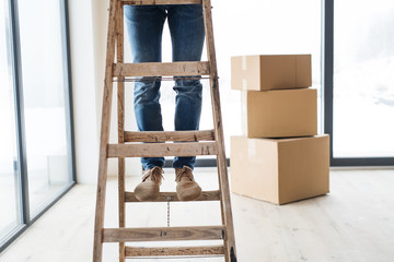 A midsection of man with cardboard boxes standing on a ladder, furnishing new house.