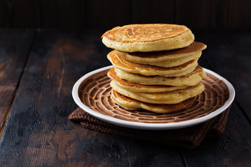 Stack of homemade little pancakes with honey, fresh raspberries and red currants on an old wooden background. Selective focus.
