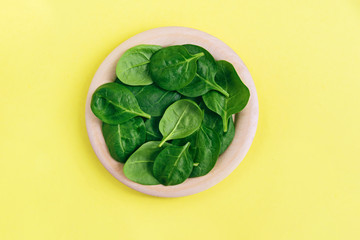 Green fresh vegetarian salad leaves on wooden plate on yellow background.