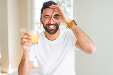 Handsome hispanic man drinking healthy orange juice with happy face smiling doing ok sign with hand...