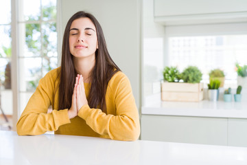Beautiful young woman wearing yellow sweater begging and praying with hands together with hope...