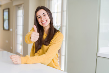 Beautiful young woman wearing yellow sweater doing happy thumbs up gesture with hand. Approving expression looking at the camera with showing success.