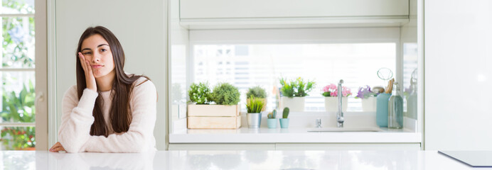 Wide angle picture of beautiful young woman sitting on white table at home thinking looking tired and bored with depression problems with crossed arms.