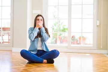 Beautiful young woman sitting on the floor at home shocked covering mouth with hands for mistake....