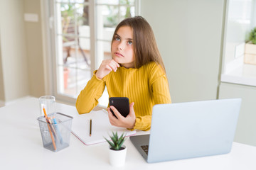 Beautiful young girl kid using smartphone and computer laptop serious face thinking about question,...