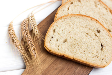 fresh sliced bread and wheat on wooden cutting board on white wooden table, top view