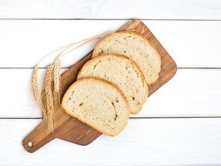 fresh sliced bread and wheat on wooden cutting board on white wooden table, top view