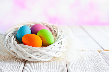Four Easter eggs in white nest on table and pink abstract background