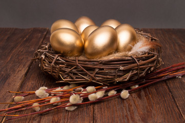 Nest with golden eggs with willow on a wooden background. Easter.